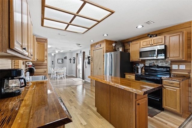 kitchen with wooden counters, sink, decorative backsplash, light wood-type flooring, and appliances with stainless steel finishes