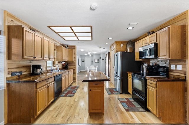 kitchen featuring sink, a center island, decorative backsplash, black appliances, and light wood-type flooring