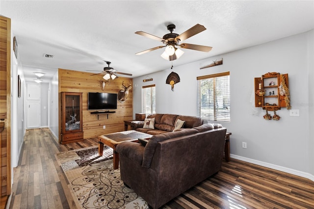 living room with a textured ceiling, dark hardwood / wood-style flooring, ceiling fan, and wood walls