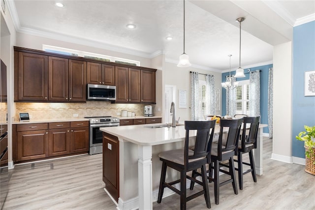 kitchen with a breakfast bar, stainless steel appliances, sink, pendant lighting, and a center island with sink