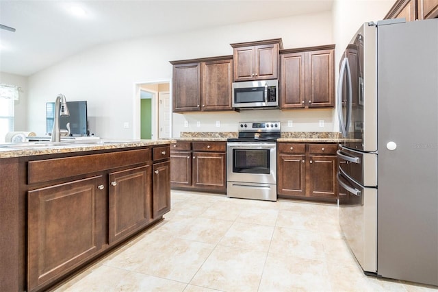 kitchen featuring sink, vaulted ceiling, light stone countertops, dark brown cabinetry, and stainless steel appliances