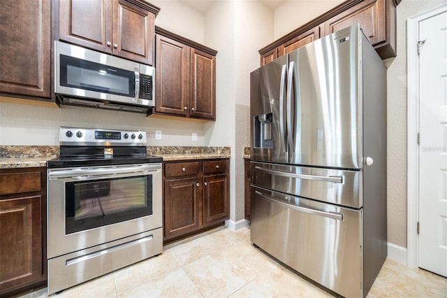 kitchen with dark brown cabinetry, light stone countertops, light tile patterned flooring, and stainless steel appliances