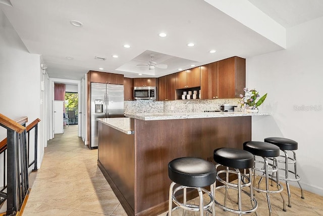 kitchen with ceiling fan, tasteful backsplash, kitchen peninsula, a breakfast bar, and appliances with stainless steel finishes