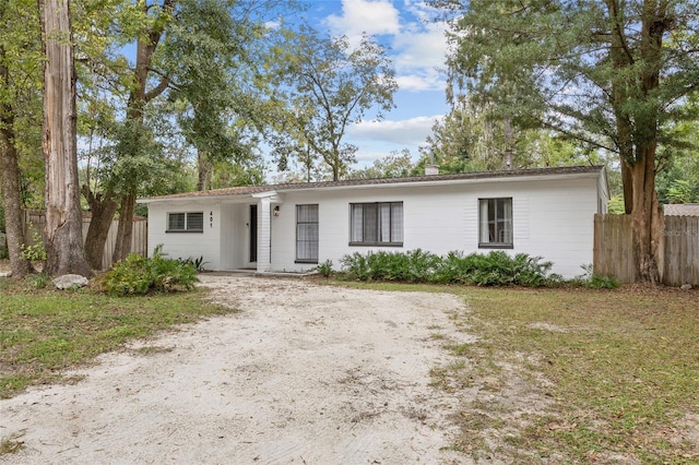 ranch-style house with dirt driveway and fence