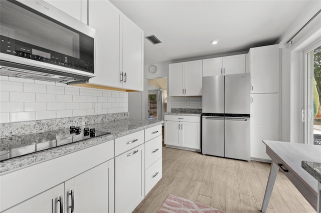 kitchen with decorative backsplash, light stone counters, stainless steel appliances, light hardwood / wood-style floors, and white cabinetry