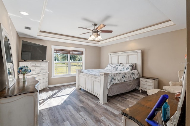 bedroom featuring ceiling fan, a raised ceiling, crown molding, and light hardwood / wood-style floors