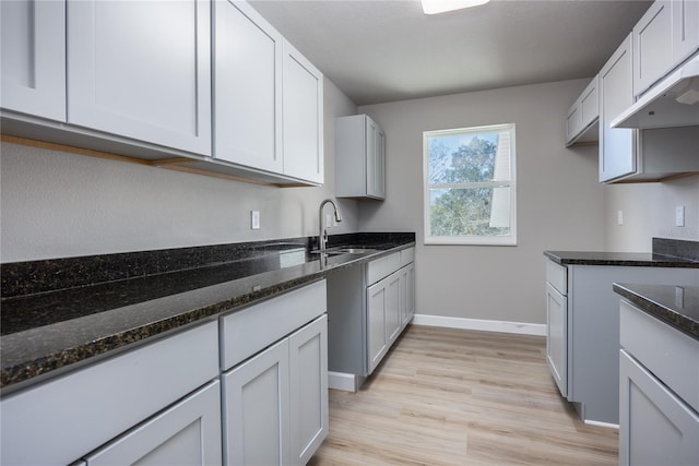 kitchen with dark stone countertops, sink, white cabinets, and light hardwood / wood-style floors