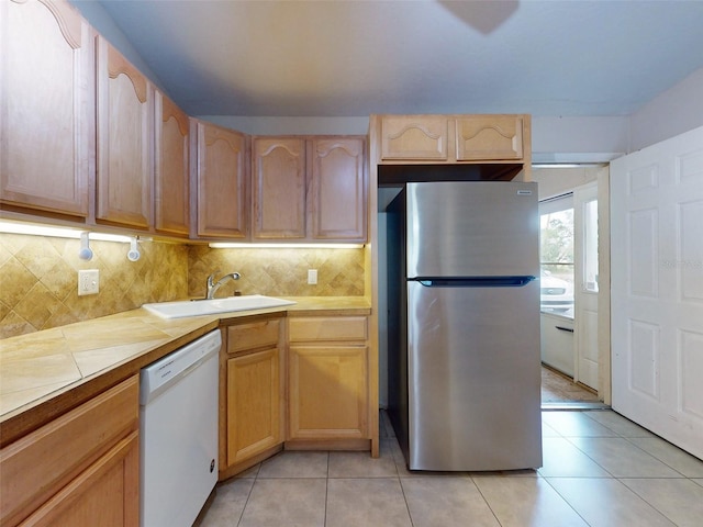 kitchen with light brown cabinetry, white dishwasher, stainless steel refrigerator, and sink