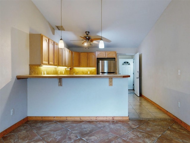 kitchen featuring ceiling fan, tasteful backsplash, stainless steel fridge, decorative light fixtures, and a breakfast bar