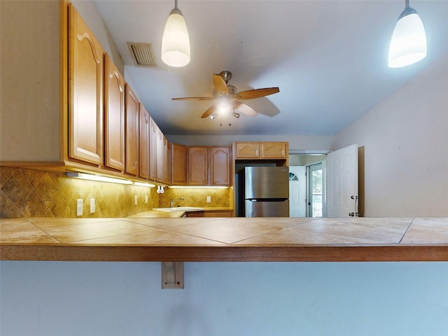 kitchen with stainless steel refrigerator, ceiling fan, tasteful backsplash, tile countertops, and pendant lighting