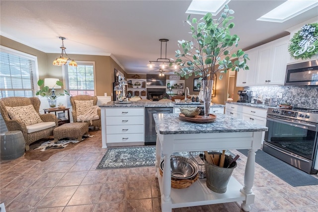 kitchen with ornamental molding, stainless steel appliances, white cabinets, a kitchen island, and hanging light fixtures