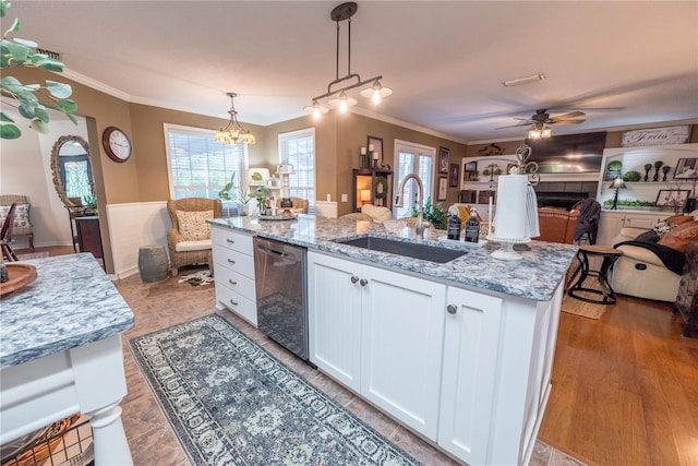 kitchen with light stone counters, stainless steel dishwasher, decorative light fixtures, white cabinets, and an island with sink