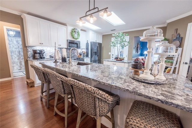 kitchen featuring a skylight, white cabinetry, sink, stainless steel appliances, and dark hardwood / wood-style flooring