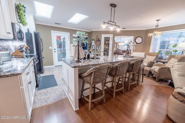 kitchen featuring appliances with stainless steel finishes, a skylight, wood-type flooring, white cabinetry, and hanging light fixtures