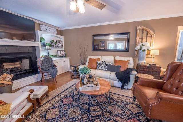 living room with hardwood / wood-style floors, ceiling fan, crown molding, and a tiled fireplace