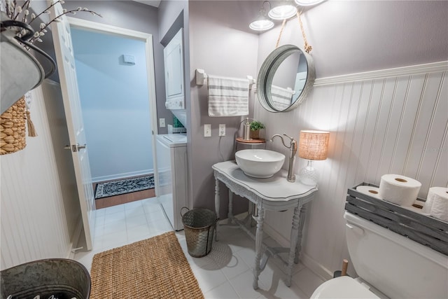 bathroom with tile patterned flooring, toilet, stacked washing maching and dryer, and sink