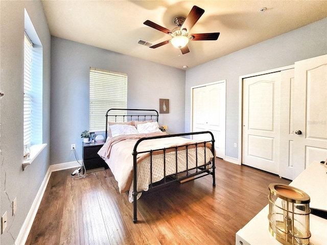 bedroom with two closets, dark hardwood / wood-style floors, and ceiling fan