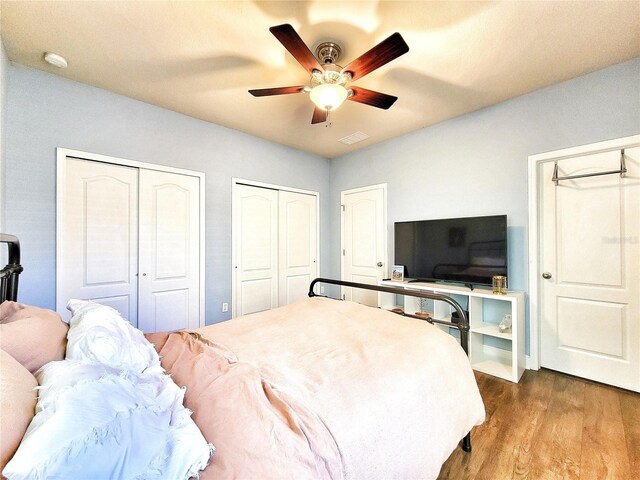 bedroom featuring ceiling fan, hardwood / wood-style floors, and two closets