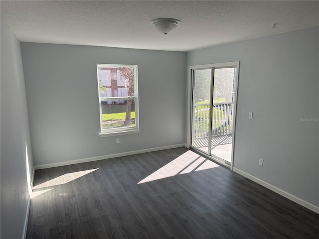 empty room featuring a textured ceiling, plenty of natural light, and dark hardwood / wood-style floors