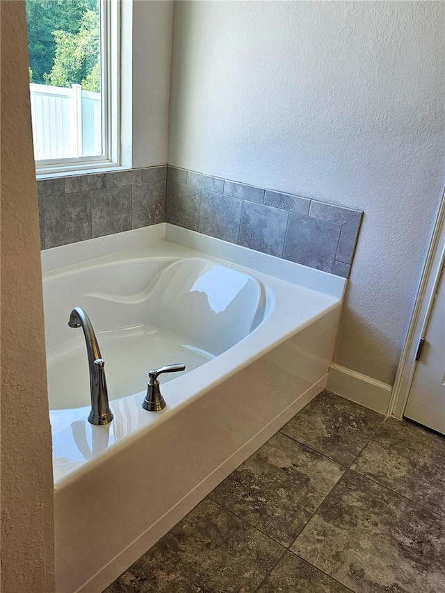 bathroom featuring baseboards, a bath, and a textured wall