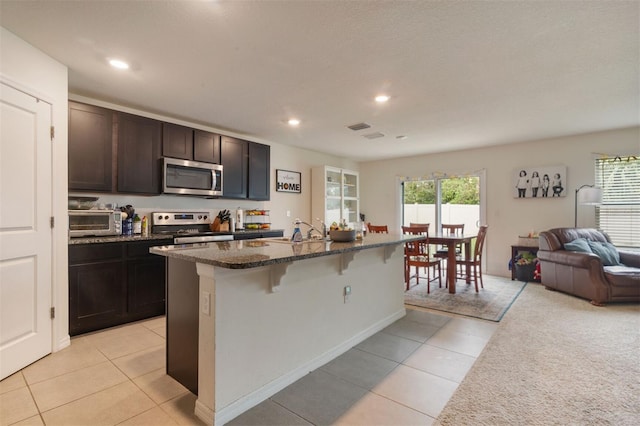 kitchen featuring a kitchen island with sink, a breakfast bar, light tile patterned floors, and appliances with stainless steel finishes