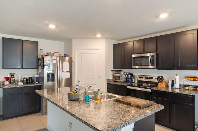 kitchen featuring a textured ceiling, stainless steel appliances, sink, light tile patterned floors, and an island with sink