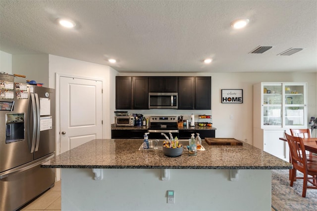 kitchen featuring a kitchen bar, a kitchen island with sink, stainless steel appliances, and a textured ceiling