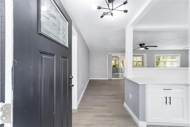 foyer entrance featuring ceiling fan with notable chandelier, a textured ceiling, and light hardwood / wood-style floors