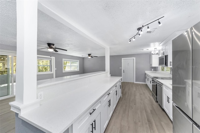 kitchen featuring white cabinets, appliances with stainless steel finishes, light wood-type flooring, and a textured ceiling