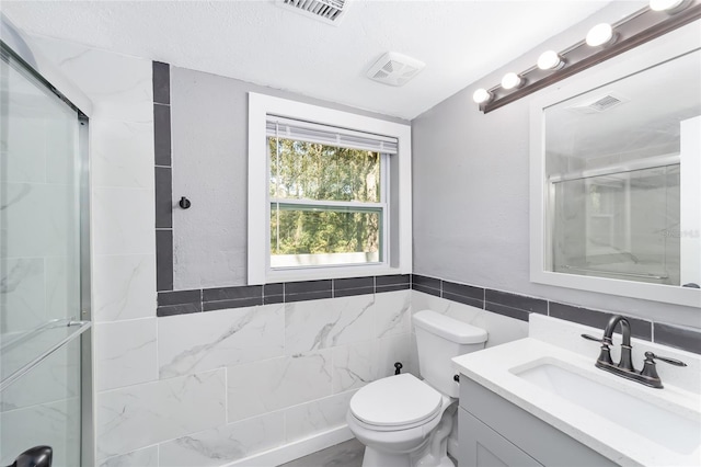 bathroom featuring a shower with door, vanity, tile walls, and toilet