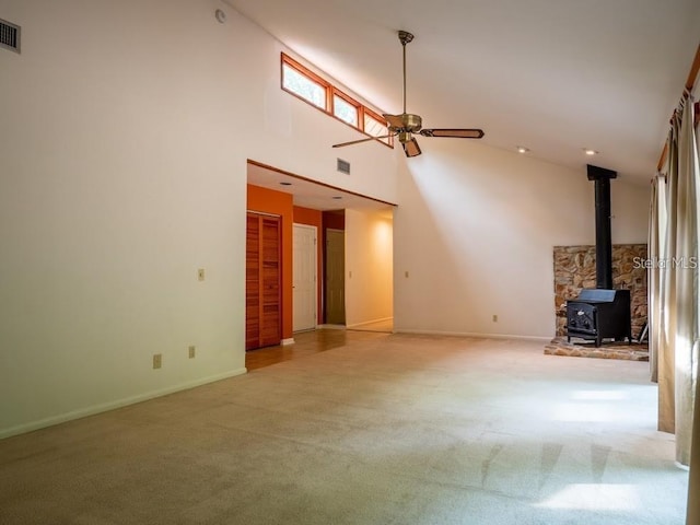 unfurnished living room with carpet, ceiling fan, a wood stove, and a high ceiling