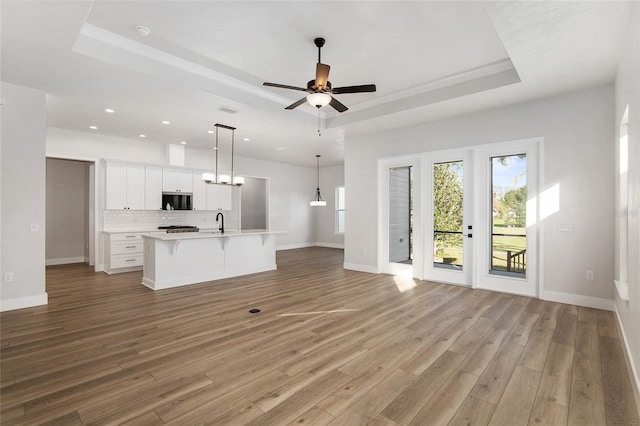 unfurnished living room featuring a raised ceiling, ceiling fan, sink, and light wood-type flooring