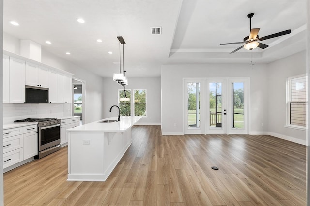 kitchen with sink, an island with sink, light hardwood / wood-style floors, white cabinets, and appliances with stainless steel finishes