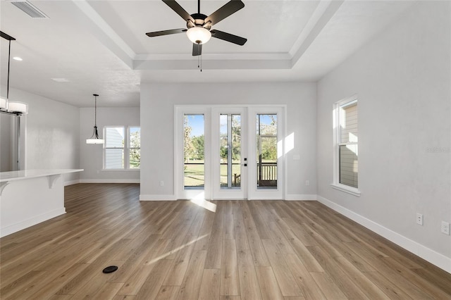 unfurnished living room featuring a tray ceiling, ceiling fan, plenty of natural light, and light wood-type flooring