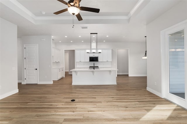 kitchen with light hardwood / wood-style floors, white cabinetry, hanging light fixtures, and an island with sink