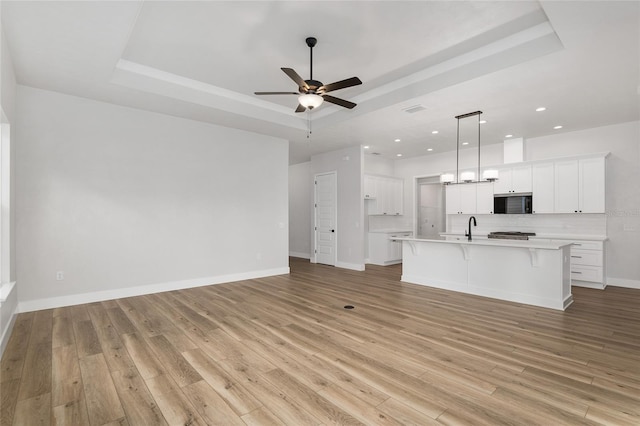 kitchen featuring a raised ceiling, light wood-type flooring, white cabinetry, and a spacious island