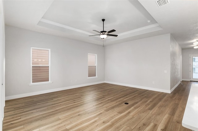 empty room featuring light wood-type flooring, a tray ceiling, and ceiling fan