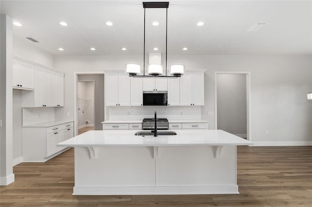 kitchen with hanging light fixtures, stainless steel appliances, white cabinetry, and a kitchen island with sink