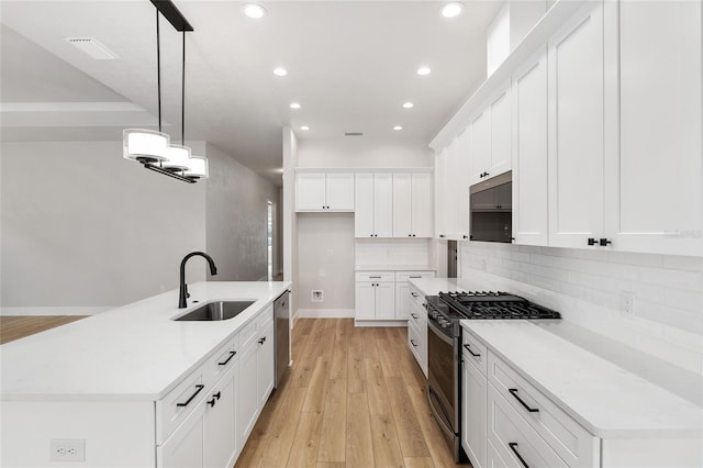 kitchen with pendant lighting, white cabinets, sink, light hardwood / wood-style flooring, and appliances with stainless steel finishes