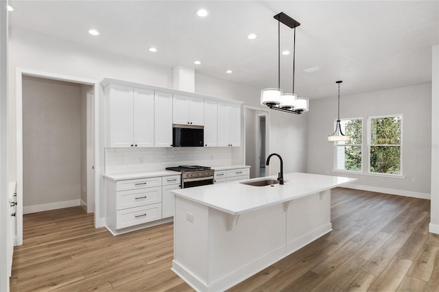 kitchen with a center island with sink, white cabinets, sink, light hardwood / wood-style flooring, and appliances with stainless steel finishes