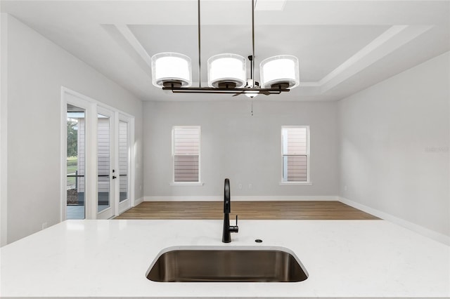 kitchen featuring light wood-type flooring, a tray ceiling, an inviting chandelier, and sink