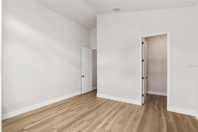 unfurnished bedroom with a walk in closet, a closet, light hardwood / wood-style flooring, and lofted ceiling