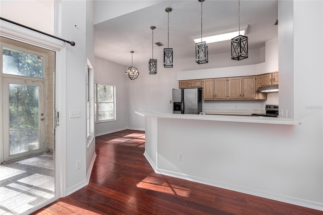 kitchen featuring dark hardwood / wood-style floors, a towering ceiling, appliances with stainless steel finishes, kitchen peninsula, and a chandelier