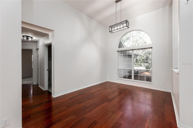 empty room featuring a towering ceiling, dark wood-type flooring, and an inviting chandelier