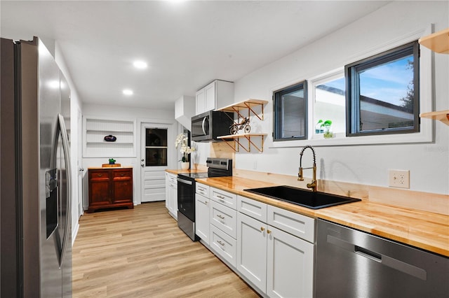 kitchen with wooden counters, appliances with stainless steel finishes, sink, light hardwood / wood-style flooring, and white cabinets