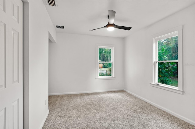 empty room with a wealth of natural light, carpet, and ceiling fan