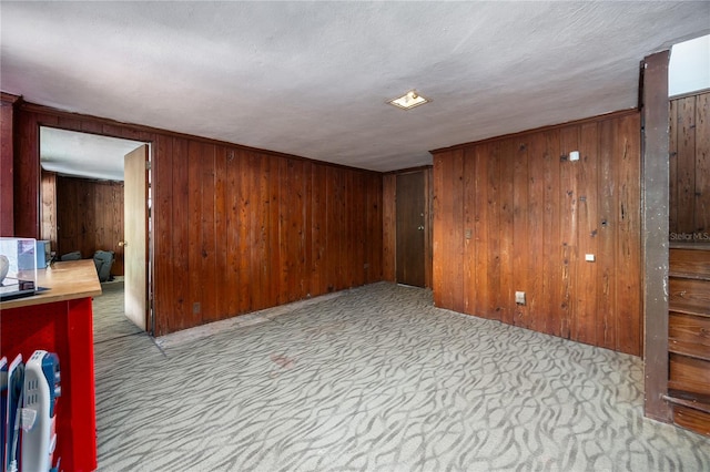 carpeted spare room with wood walls and a textured ceiling