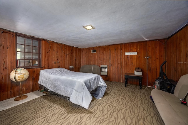 carpeted bedroom with a textured ceiling, heating unit, and wooden walls