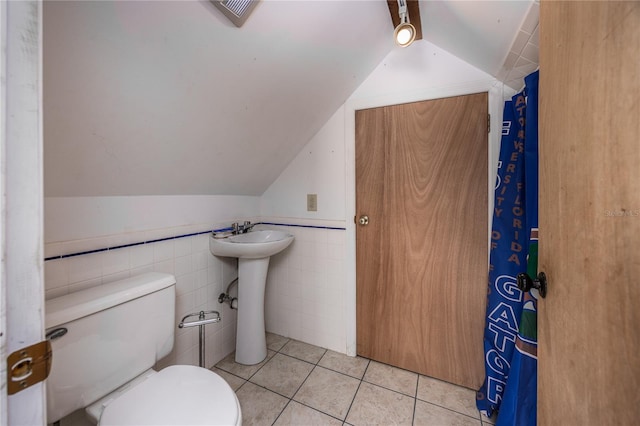 bathroom with tile patterned floors, vaulted ceiling, sink, tile walls, and toilet