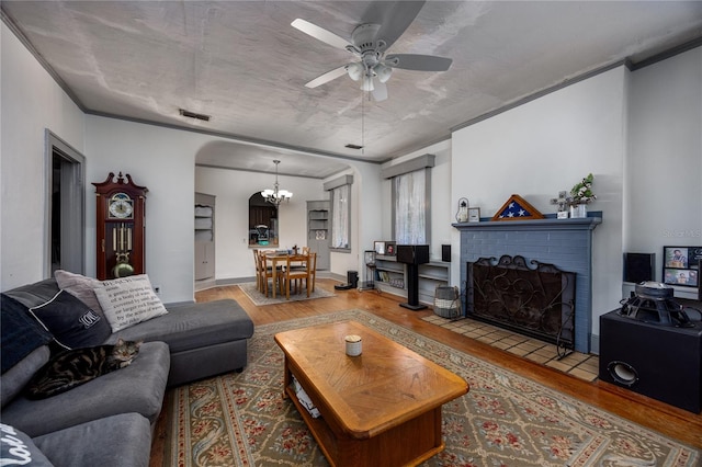 living room with ceiling fan with notable chandelier, crown molding, wood-type flooring, and a fireplace